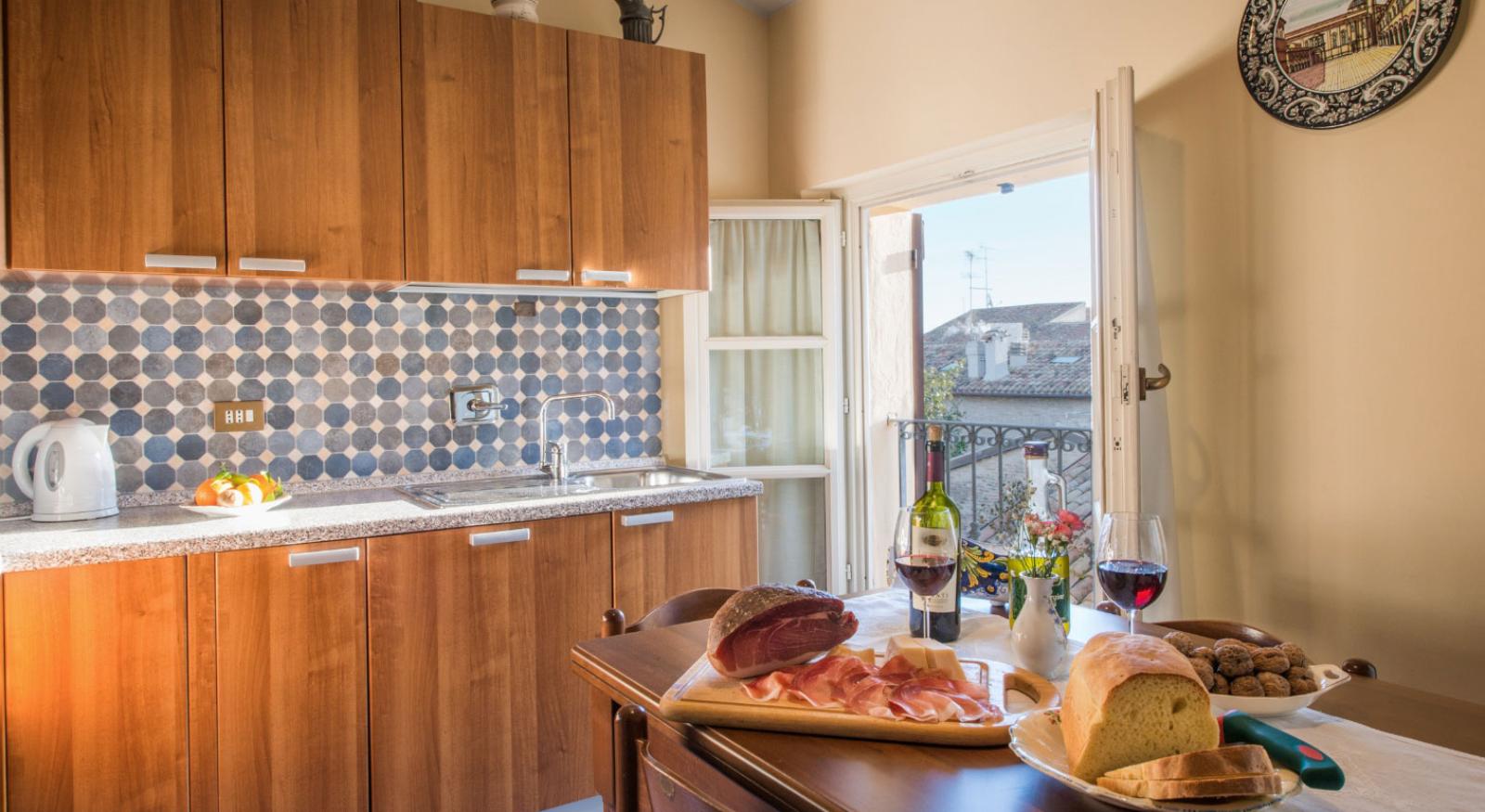 Cucina accogliente con cibo e vino, affacciata su un balcone soleggiato.