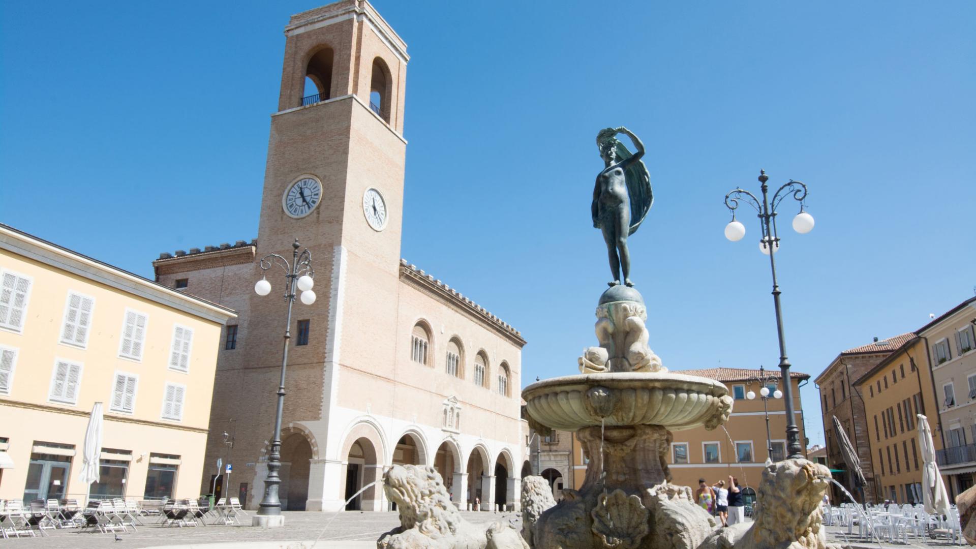 Piazza con fontana e torre dell'orologio in una città italiana.