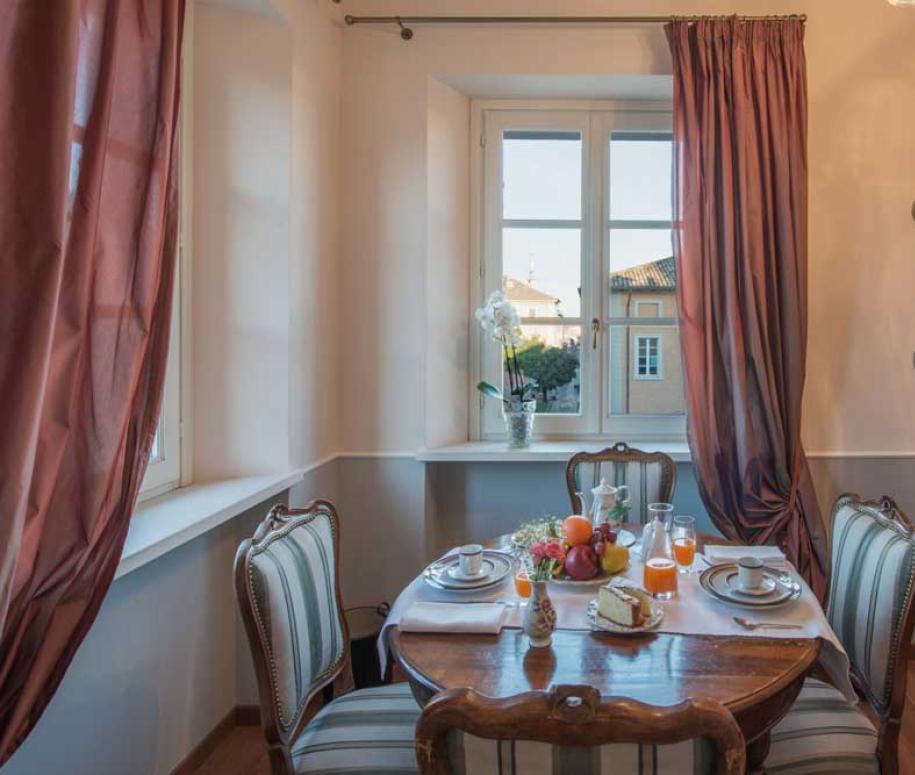 Sala da pranzo accogliente con tavolo apparecchiato, divano rosso e finestra luminosa.