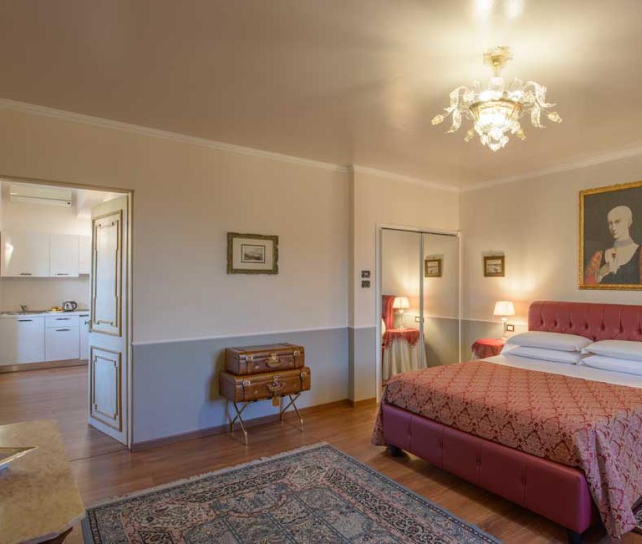 Camera da letto elegante con letto matrimoniale, tappeto e lampadario, cucina adiacente.
