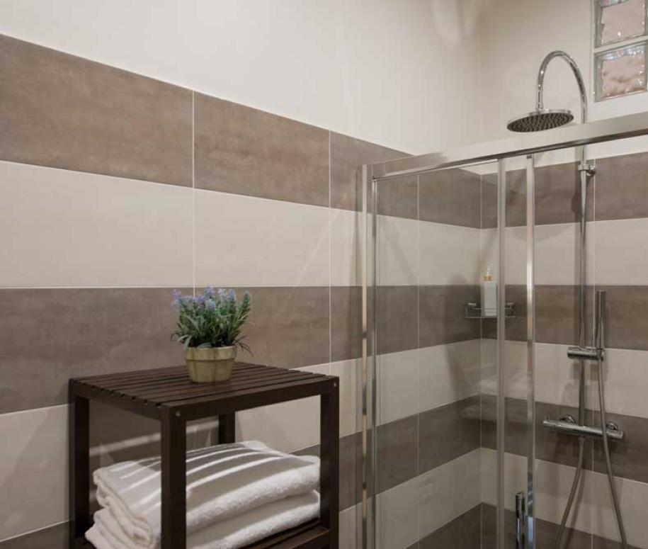 Bagno moderno con doccia, piastrelle a strisce e scaffale con asciugamani.