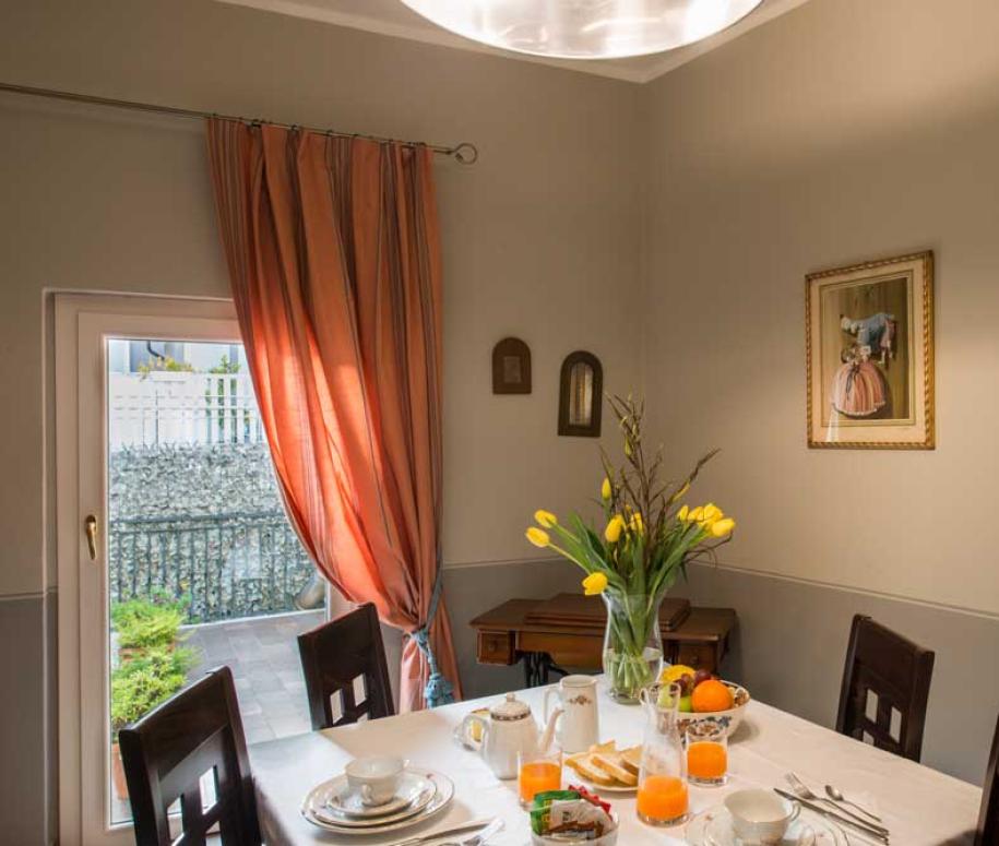 Sala da pranzo luminosa con tavolo apparecchiato e fiori gialli in vaso.