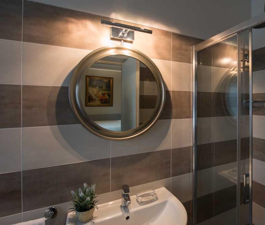 Bagno moderno con doccia, specchio rotondo e piastrelle a strisce orizzontali.