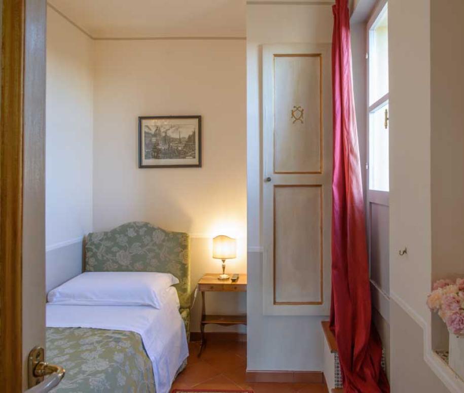 Camera accogliente con letto singolo, lampada da tavolo e decorazioni floreali.