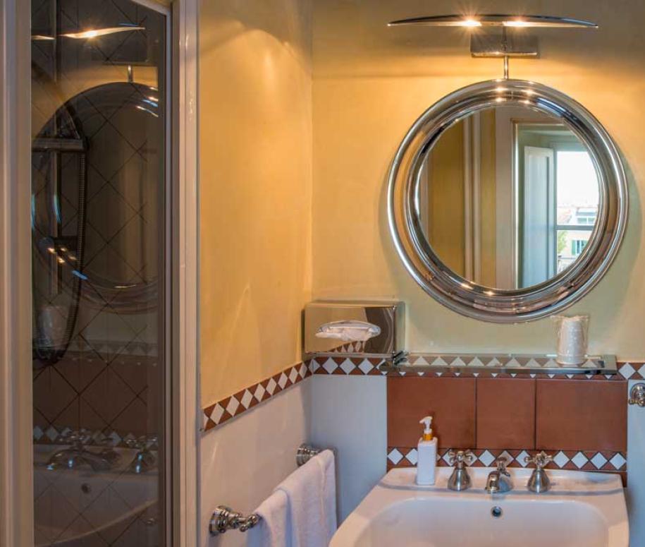 Bagno con specchio rotondo, lavandino, dispenser sapone e finestra luminosa.