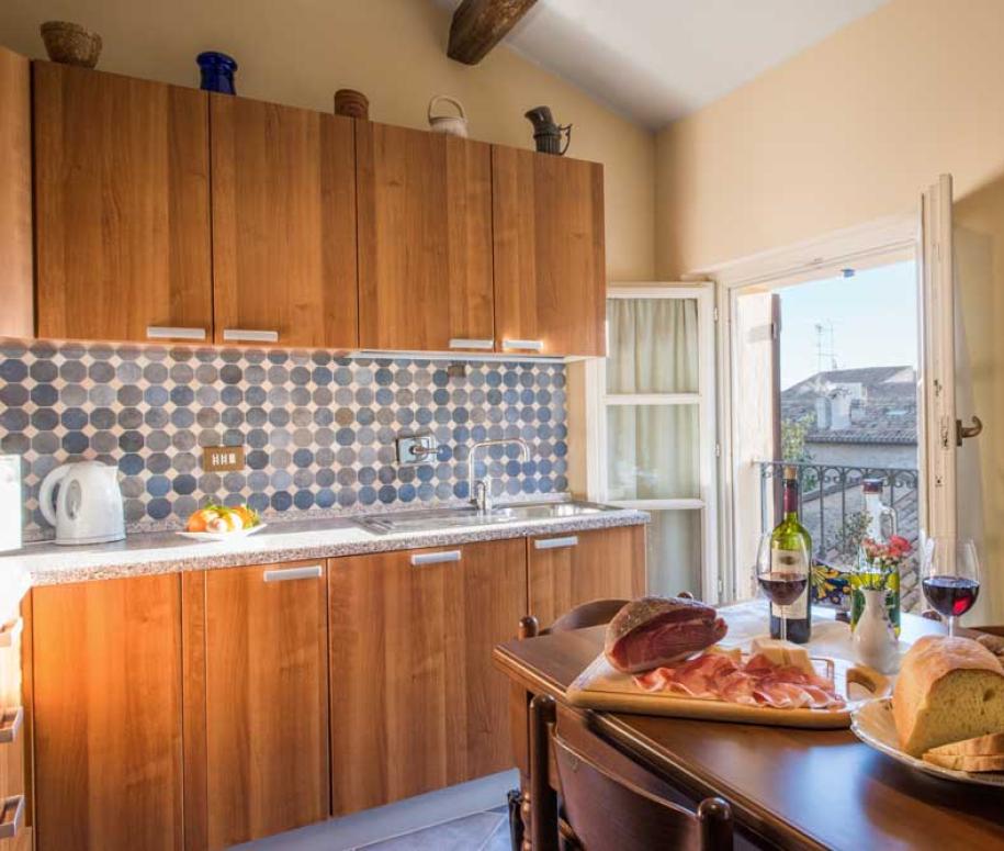 Cucina accogliente con tavolo imbandito, vino e affettati, vista dalla finestra aperta.