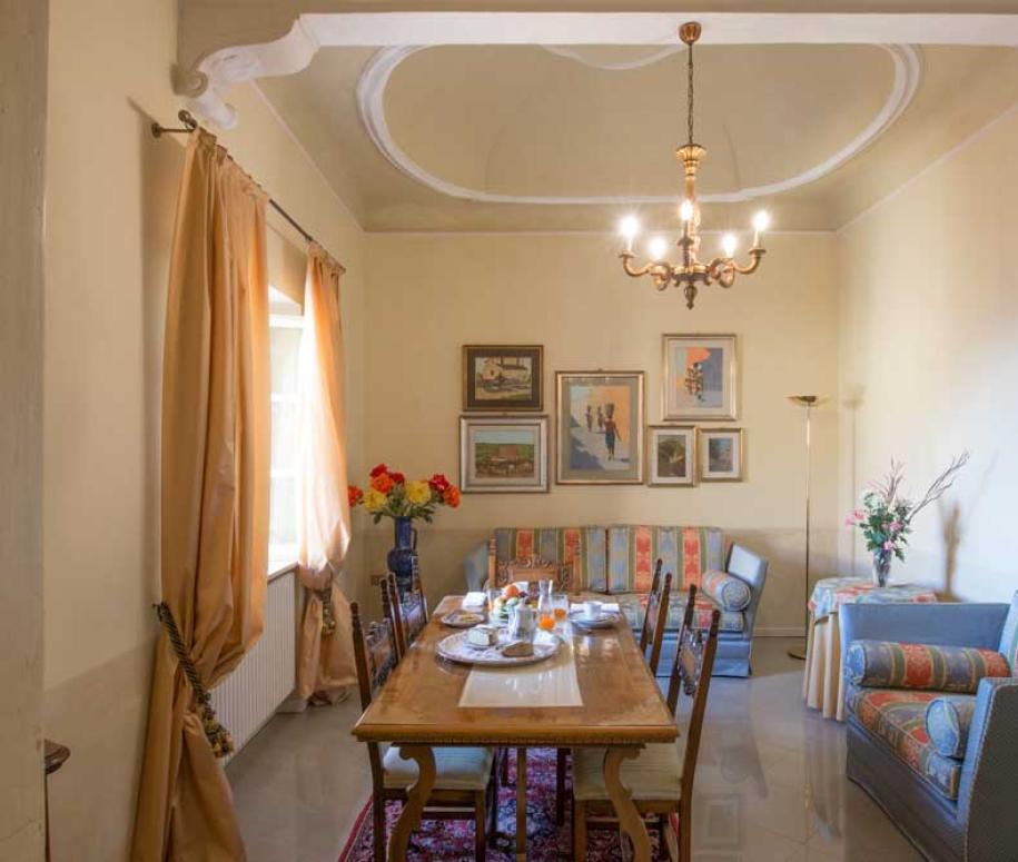 Sala da pranzo luminosa con tavolo in legno, divani colorati e opere d'arte alle pareti.