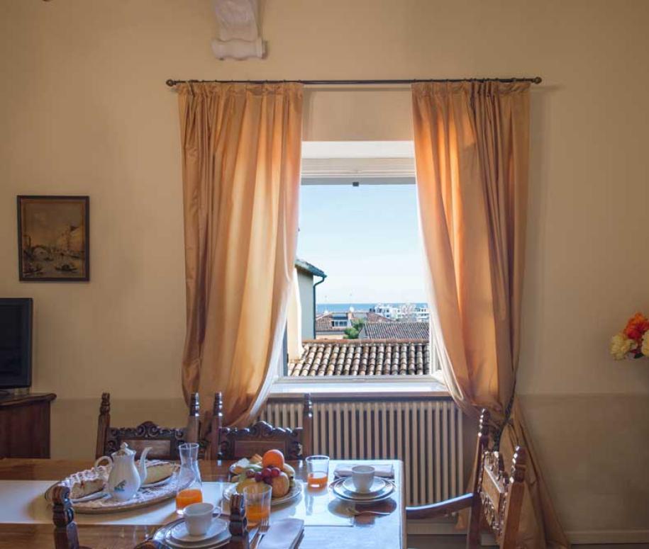 Sala da pranzo con vista sul mare, tavolo apparecchiato e fiori colorati.