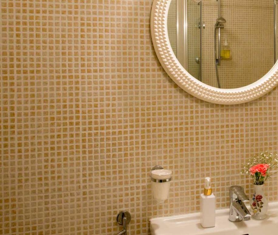 Bagno con specchio rotondo illuminato e lavandino con dispenser e fiori.