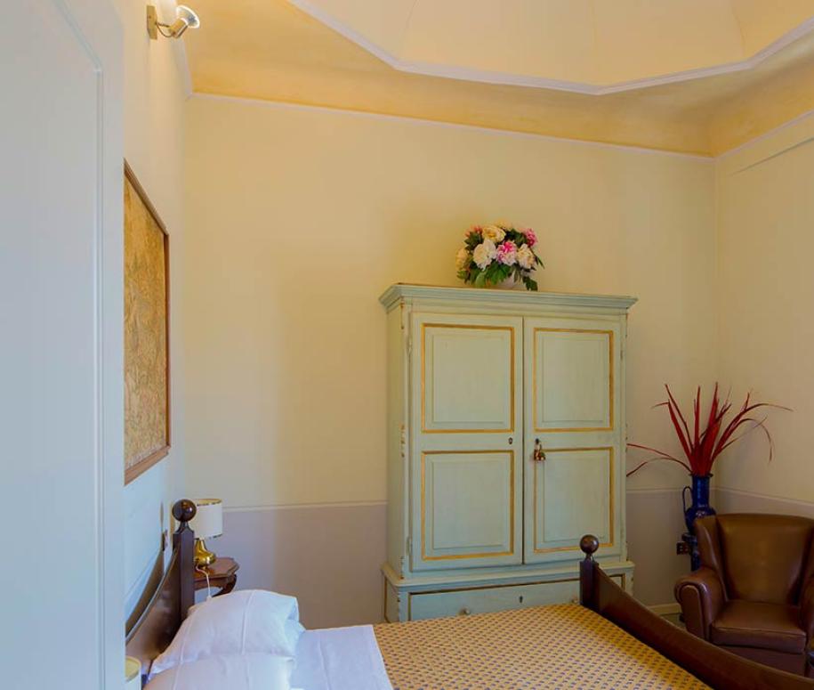 Camera accogliente con letto, armadio, poltrona e finestra con tende rosse.