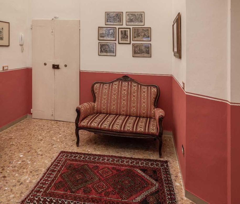 Sala d'attesa con divano antico, tappeto e quadri alle pareti.