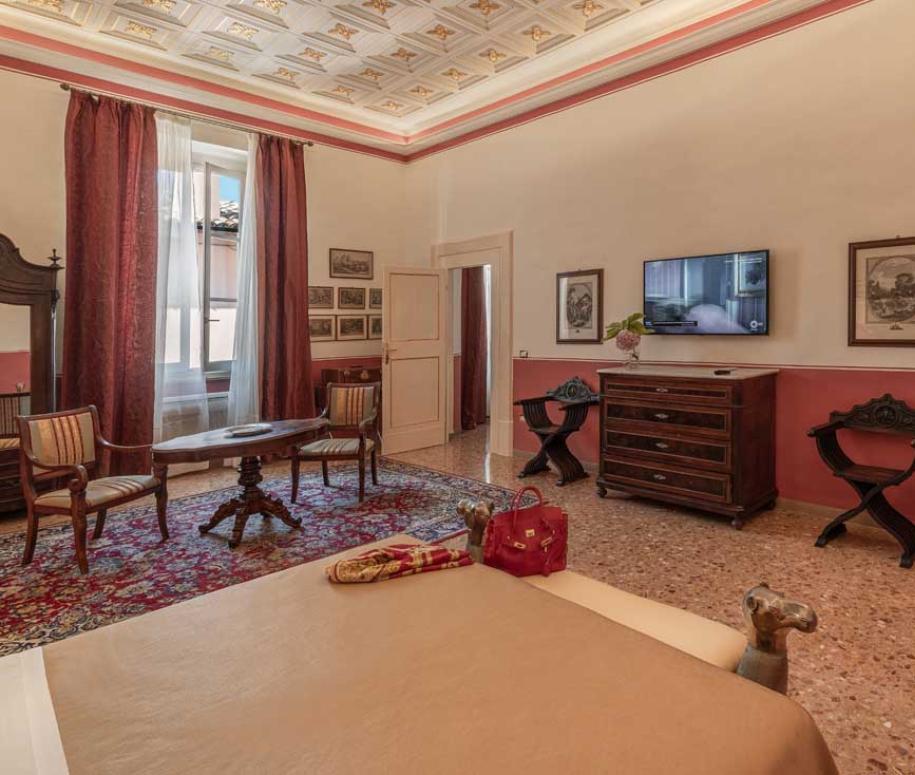Elegante camera con arredi classici, soffitto decorato e TV a parete.